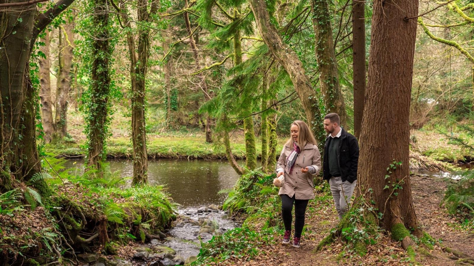 Couple walking through Glenarm Forest beside a river